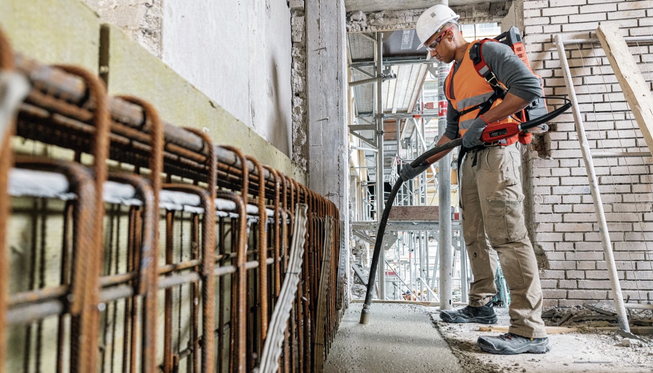 Worker using the NCV Cordless concrete vibrator indoors, vibrating a strip of concrete, free of gas fumes.